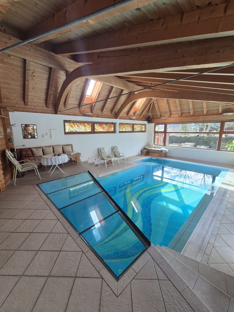 Ferienhaus mit Hallenbad: das beleuchtete Schwimmwohnzimmer mit Blick in den Garten.